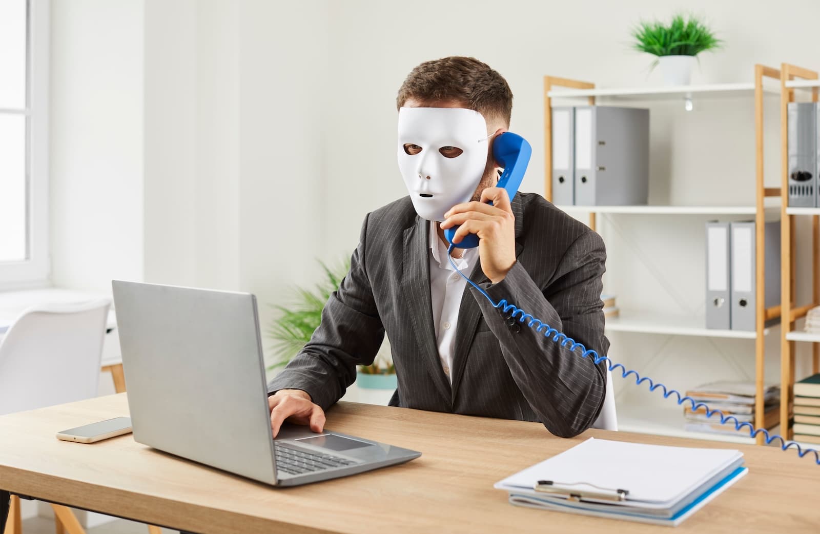 A person with face mask using a laptop and telephone