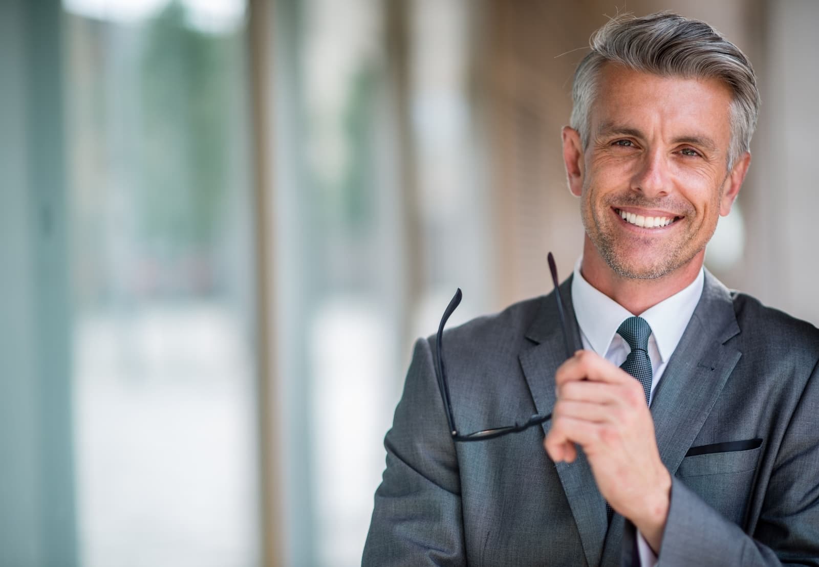 A man wearing suit and holding his glasses