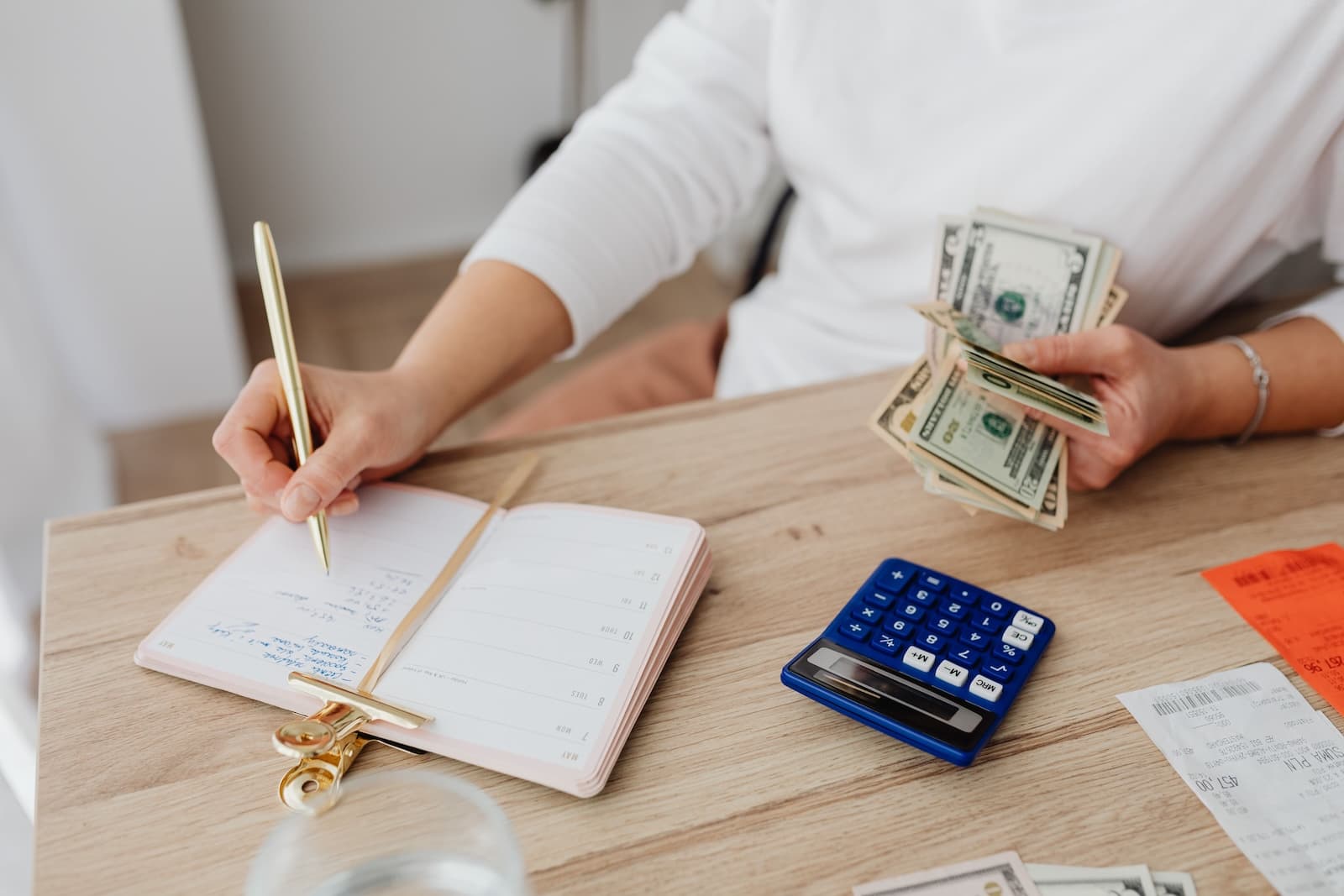 Person writing on a notebook at a desk with money on hand