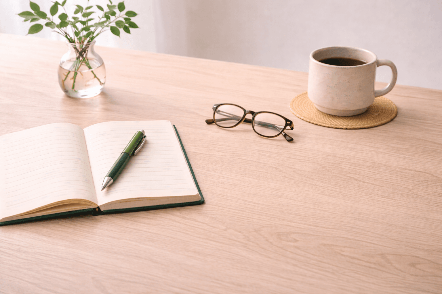 Notebook and reading glasses on a light wood desk